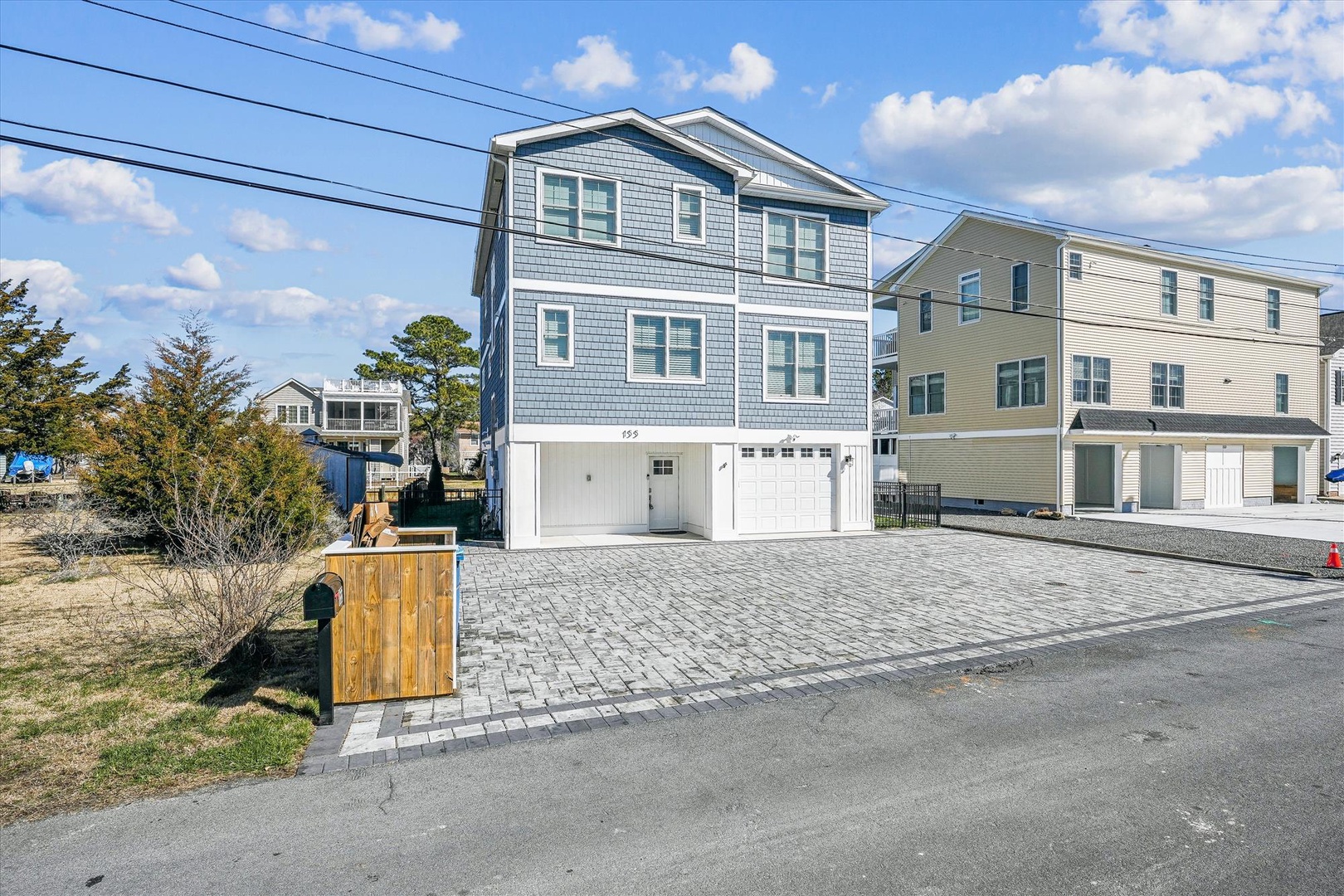 Coastal two-story home with paver stone driveway in a quiet residential neighborhood, featuring ground-level garage access.