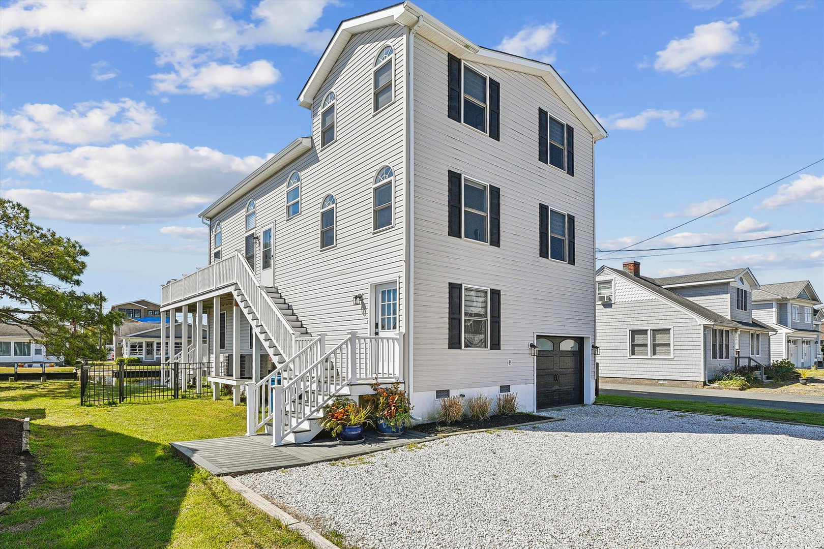 A spacious three-story beach home with classic coastal architecture, featuring white siding and black shutters, set in a quiet neighborhood near the shore.