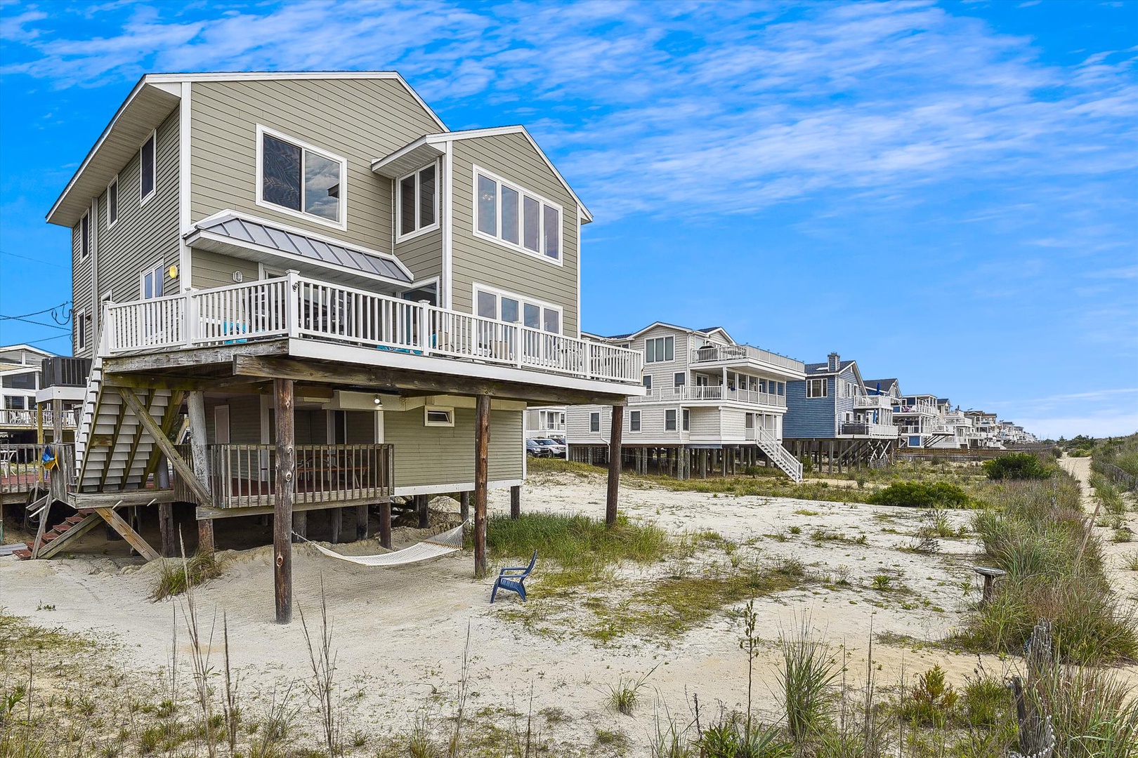 This beachfront property sits elevated on stilts amid sandy dunes and natural coastal vegetation, offering direct access to the shore and neighboring beach homes.