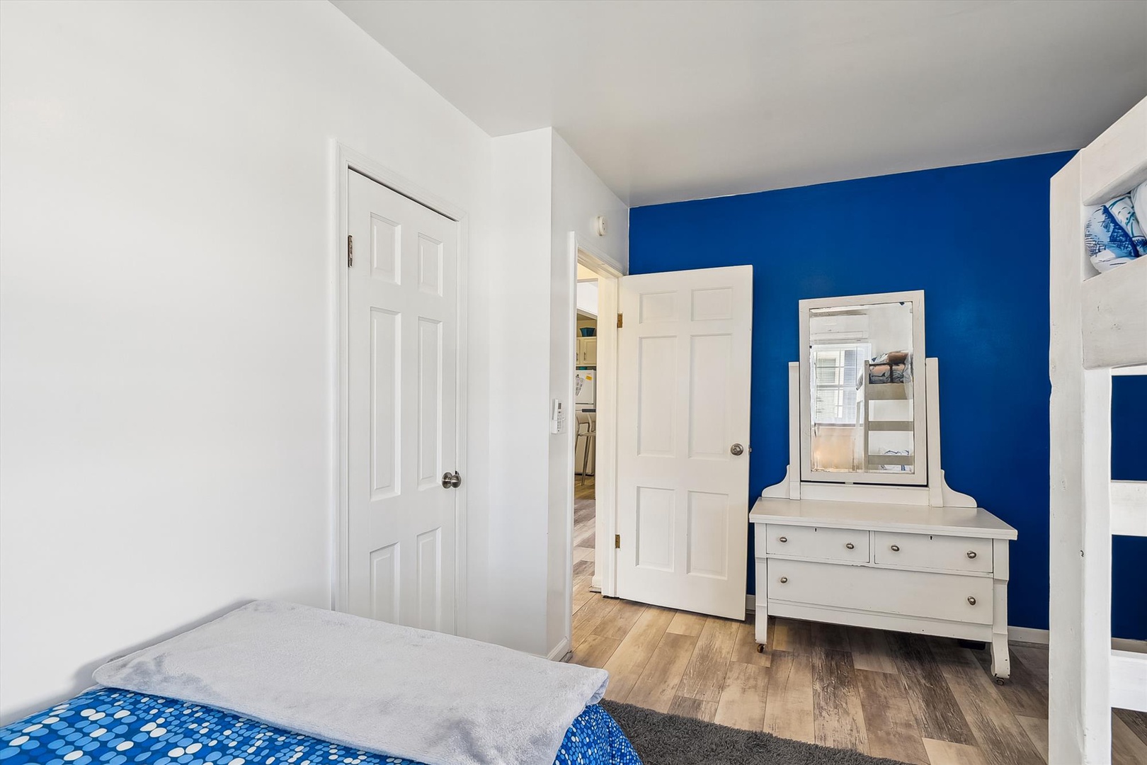 Your bright bedroom features warm hardwood floors, a crisp white dresser, and a bold blue accent wall—creating a fresh, modern space for restful nights.