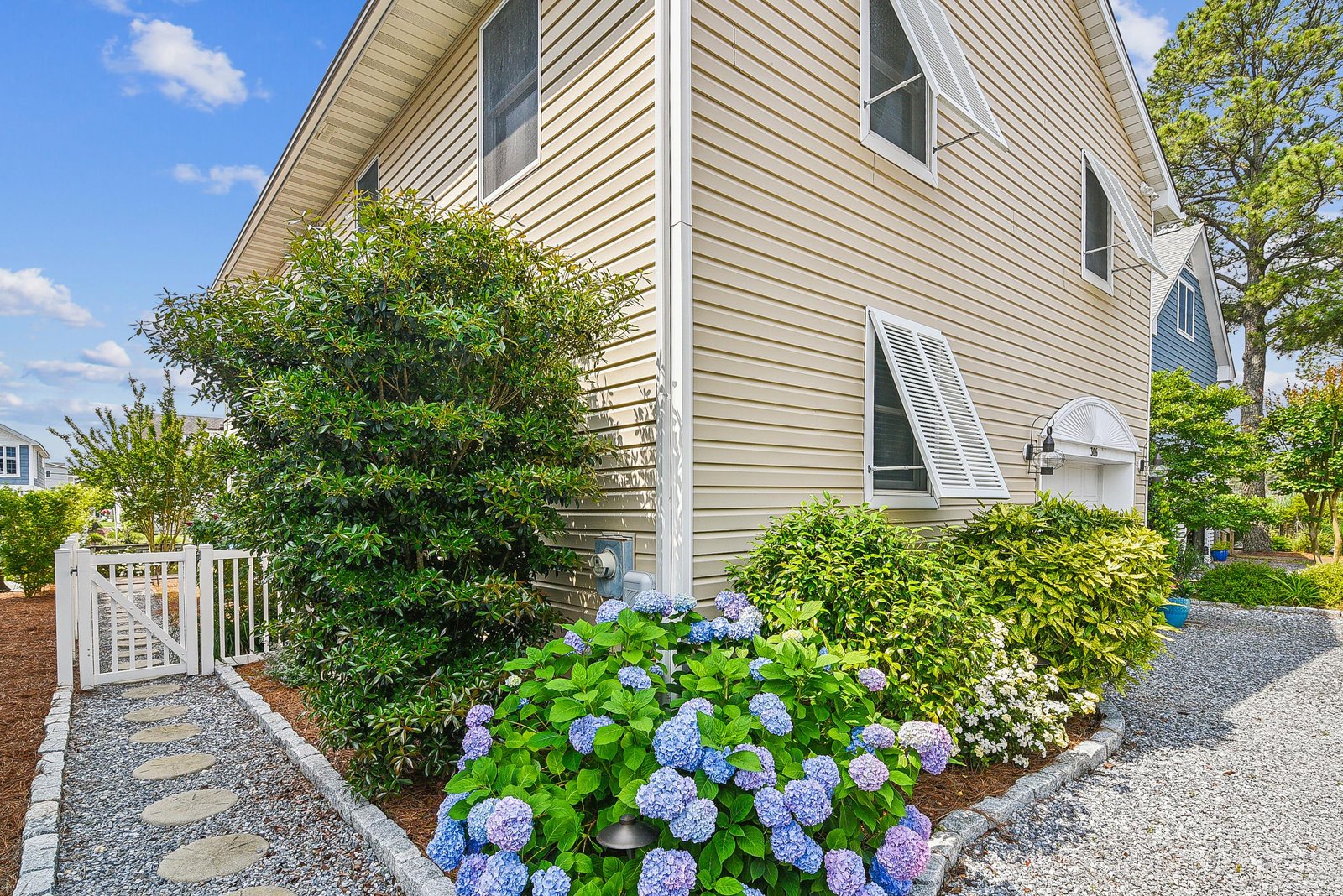The property entrance features charming landscaping with vibrant hydrangeas and a welcoming gate, set within a quiet neighborhood just steps from the front door.