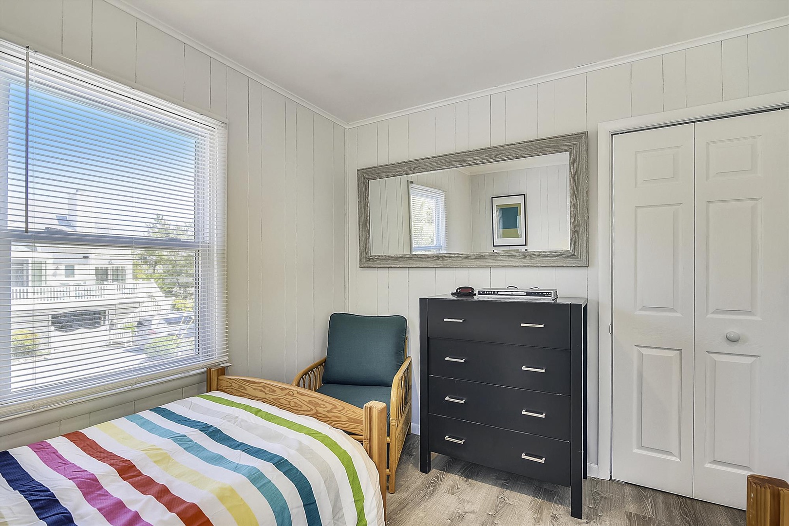 Cozy coastal bedroom with cheerful rainbow linens, plenty of natural light, and space to unpack and unwind after beach days.