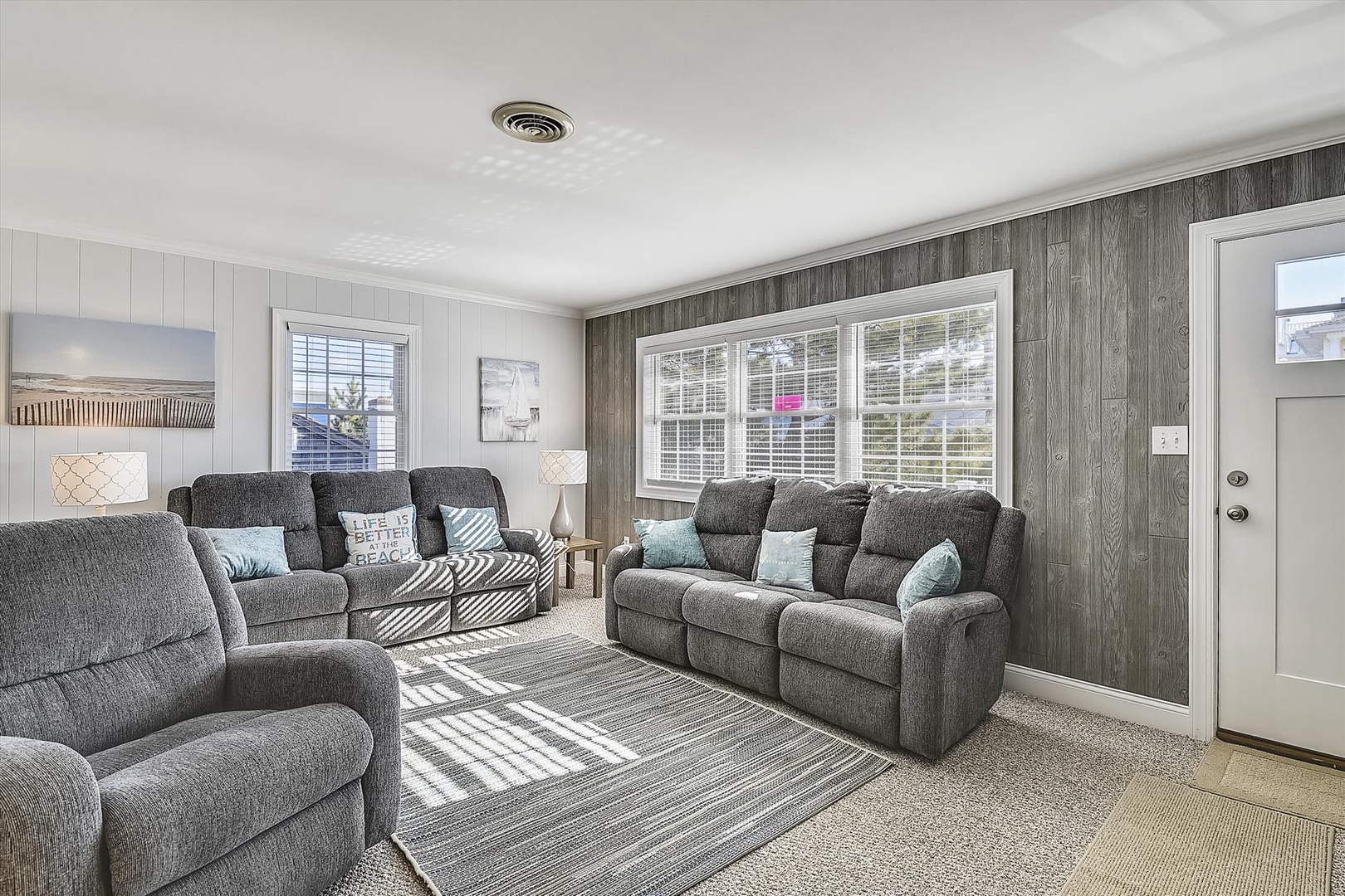 Sink into plush gray sofas surrounded by coastal-inspired decor, where natural light floods through expansive windows creating your perfect relaxation retreat.