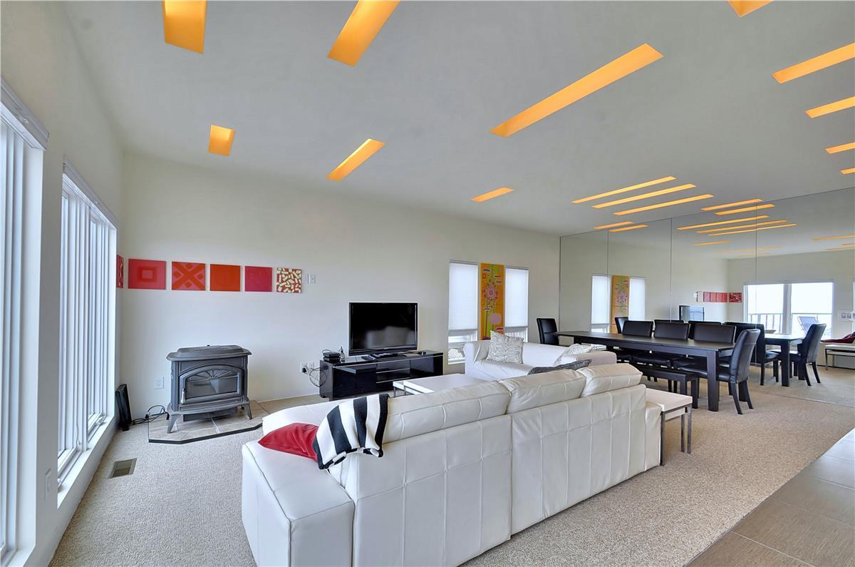 Unwind in this inviting living space with striking ceiling lights, floor-to-ceiling windows, plush seating, and an elegant dining table nearby.