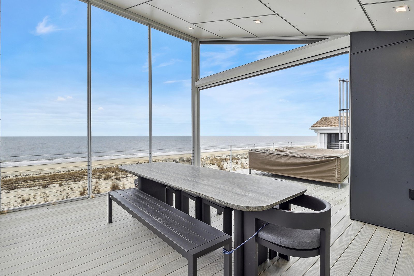 A spacious covered deck with modern dining furniture overlooks the sandy beach and calm ocean waters, offering you an ideal spot to savor meals or morning coffee with the soothing sea breeze.