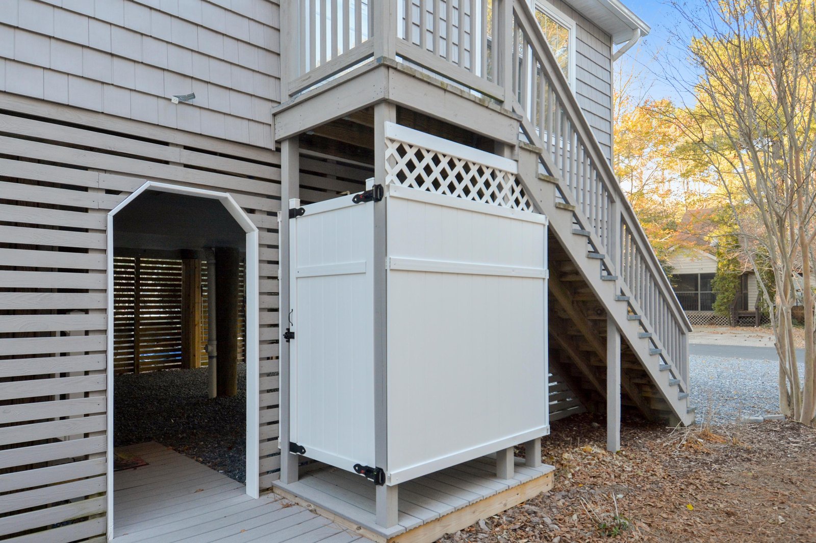 The property features a second-story balcony with stairs and lattice detailing, set amidst autumn foliage and surrounded by neighboring homes.