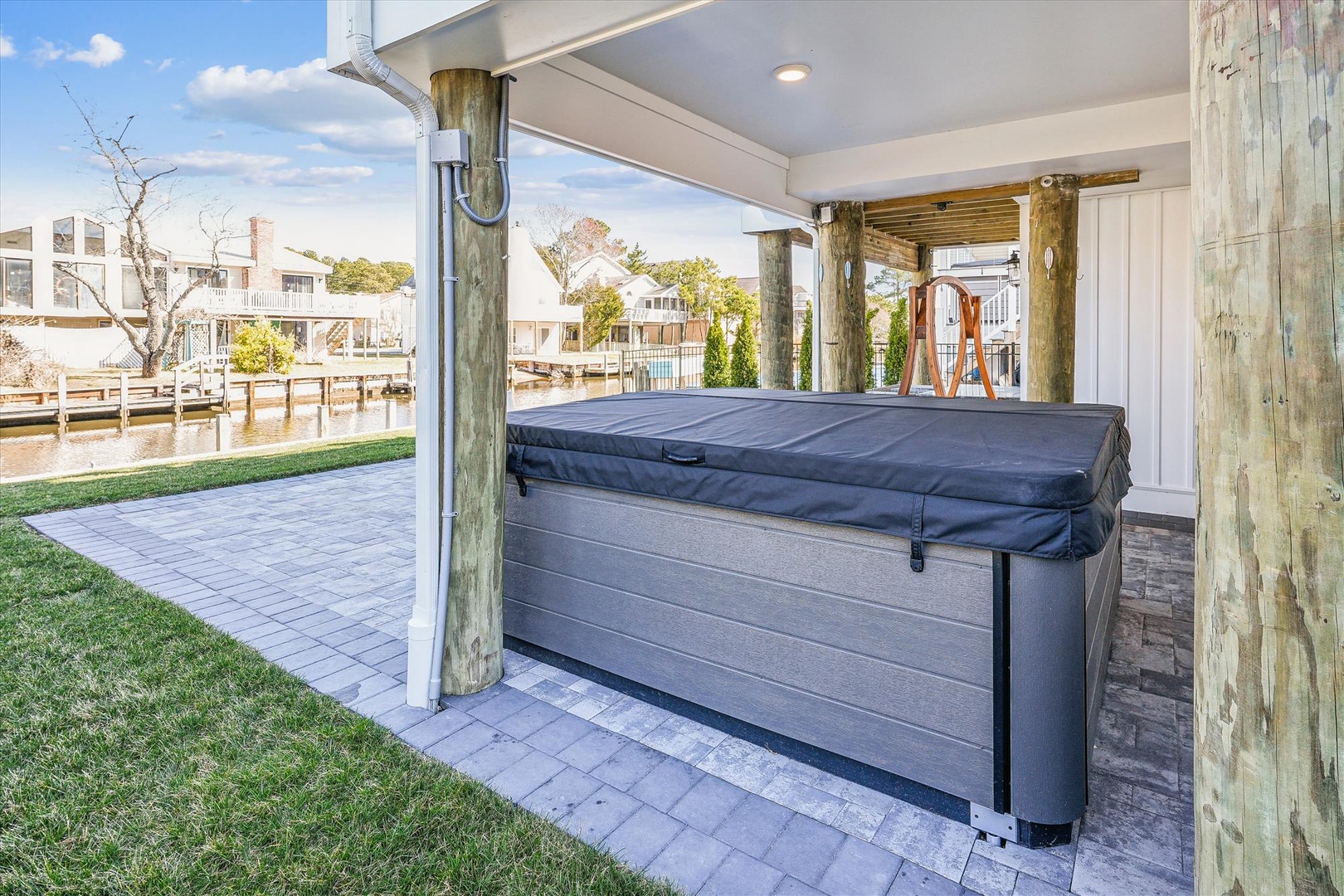 A covered outdoor hot tub overlooking the waterfront, with serene canal views and paver stone patio—perfect for unwinding after a day on the water.