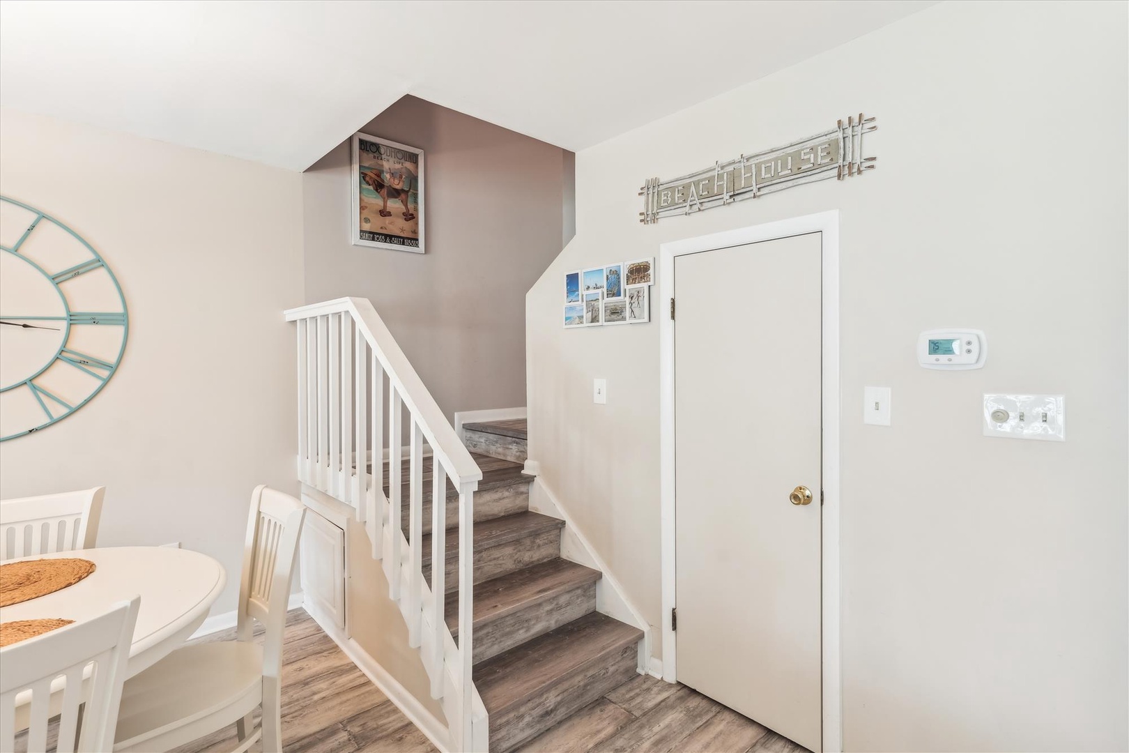 The entrance opens into a welcoming space featuring clean, bright interiors and a coastal-themed decorative touch above the door. A convenient staircase leads to upstairs accommodations.