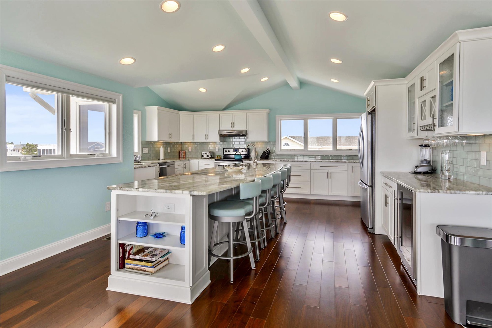 Bright coastal kitchen with gleaming granite counters, crisp white cabinetry, and a large island perfect for gathering over morning coffee or evening meals. Rich hardwood floors add warmth throughout.