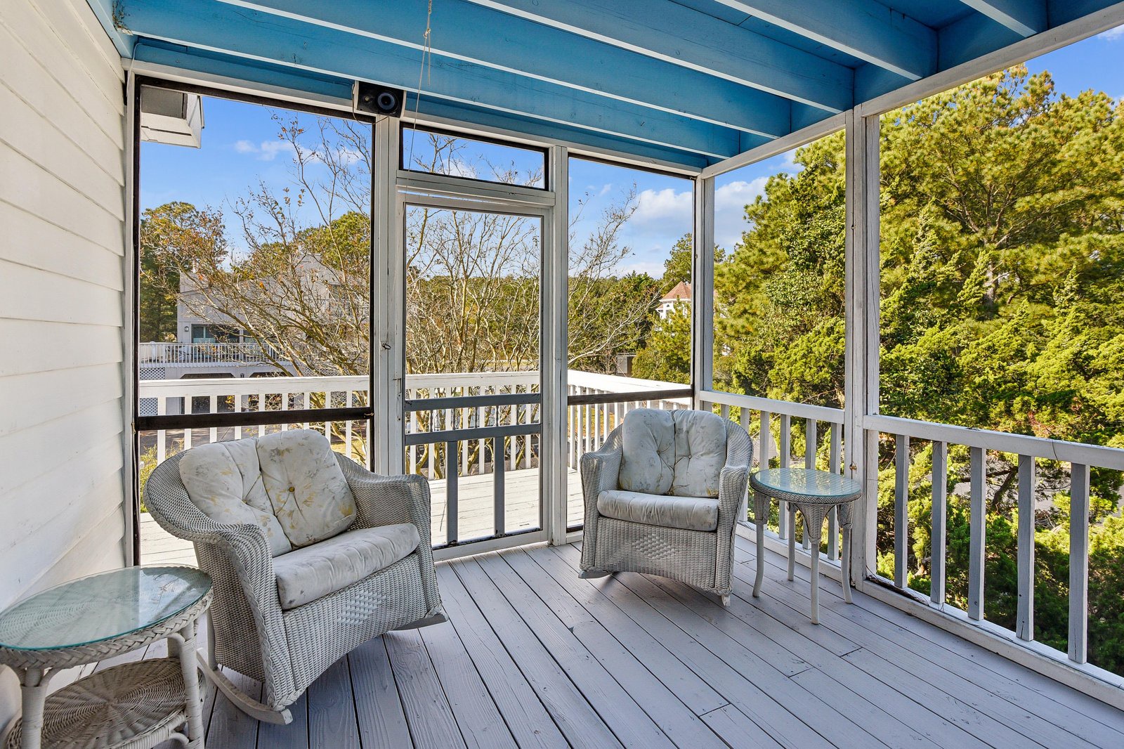 Relax in your screened porch with cozy wicker seating and peek-a-boo views of lush greenery beyond the white railings.