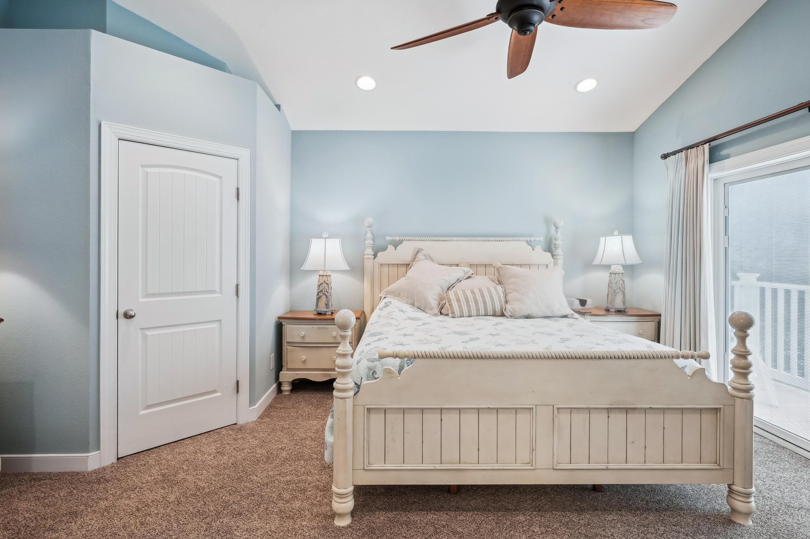 Relax in your airy bedroom, where soft blue walls and a cozy coastal-style bed invite you to unwind beneath the ceiling fan's gentle breeze.