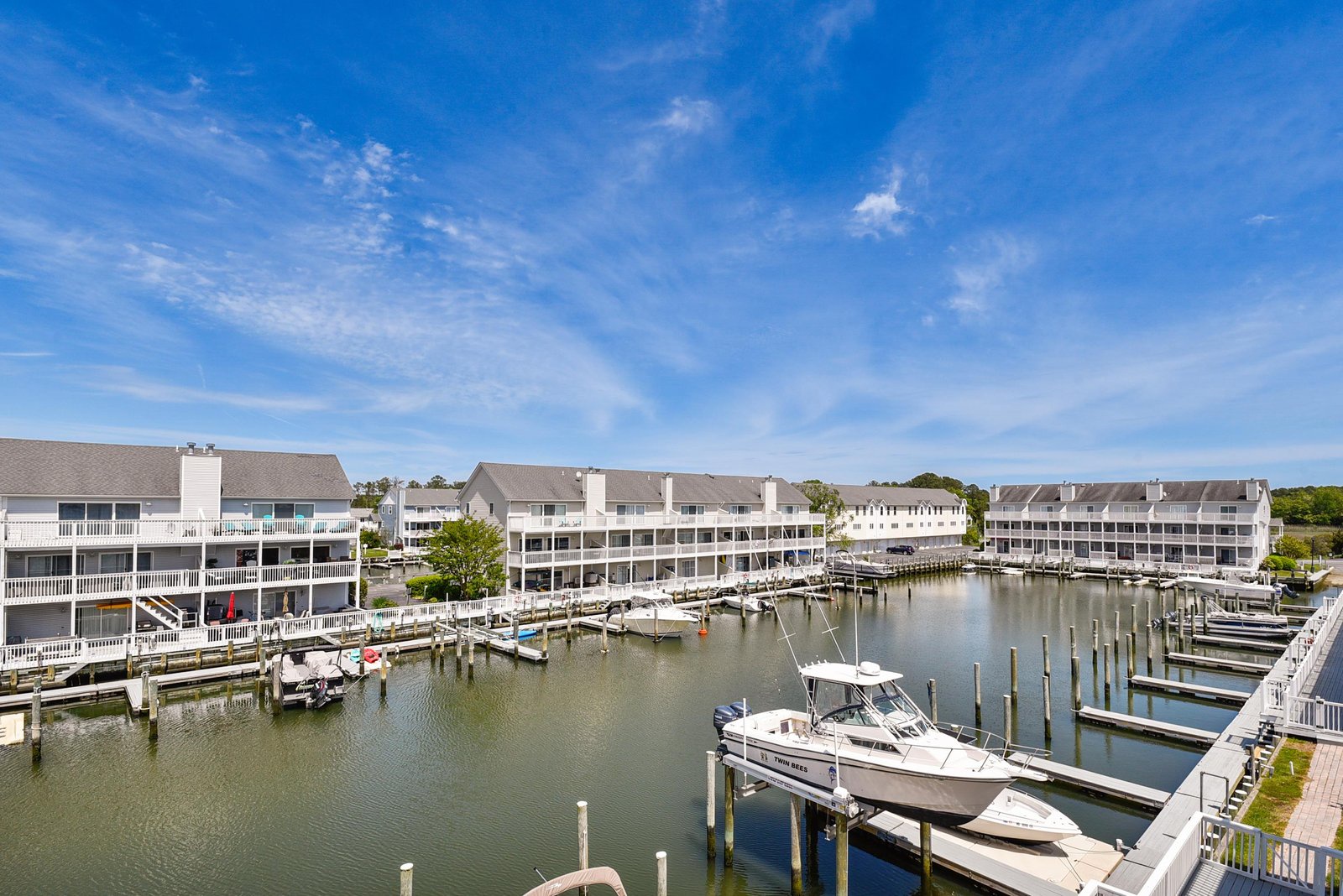 Waterfront resort community featuring marina boat slips, multi-level condominiums, and private docks along a calm harbor under expansive blue skies.