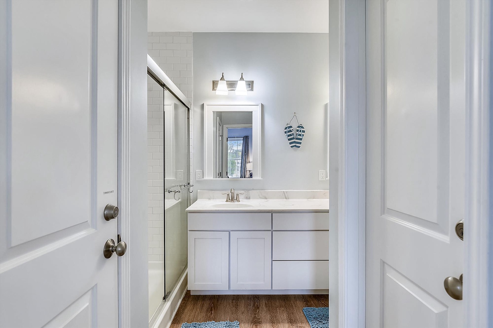 Step into your bright, spotless bathroom—white cabinetry, warm wood floors, and charming nautical touches await you after a refreshing shower.
