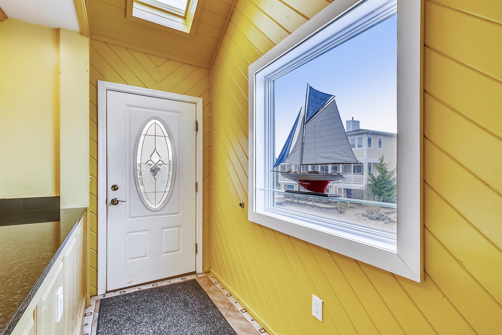 This cheerful entrance welcomes you with warm wood tones and natural light from the skylight above. The decorative door invites you inside, while the nearby window offers glimpses of the neighborhood.