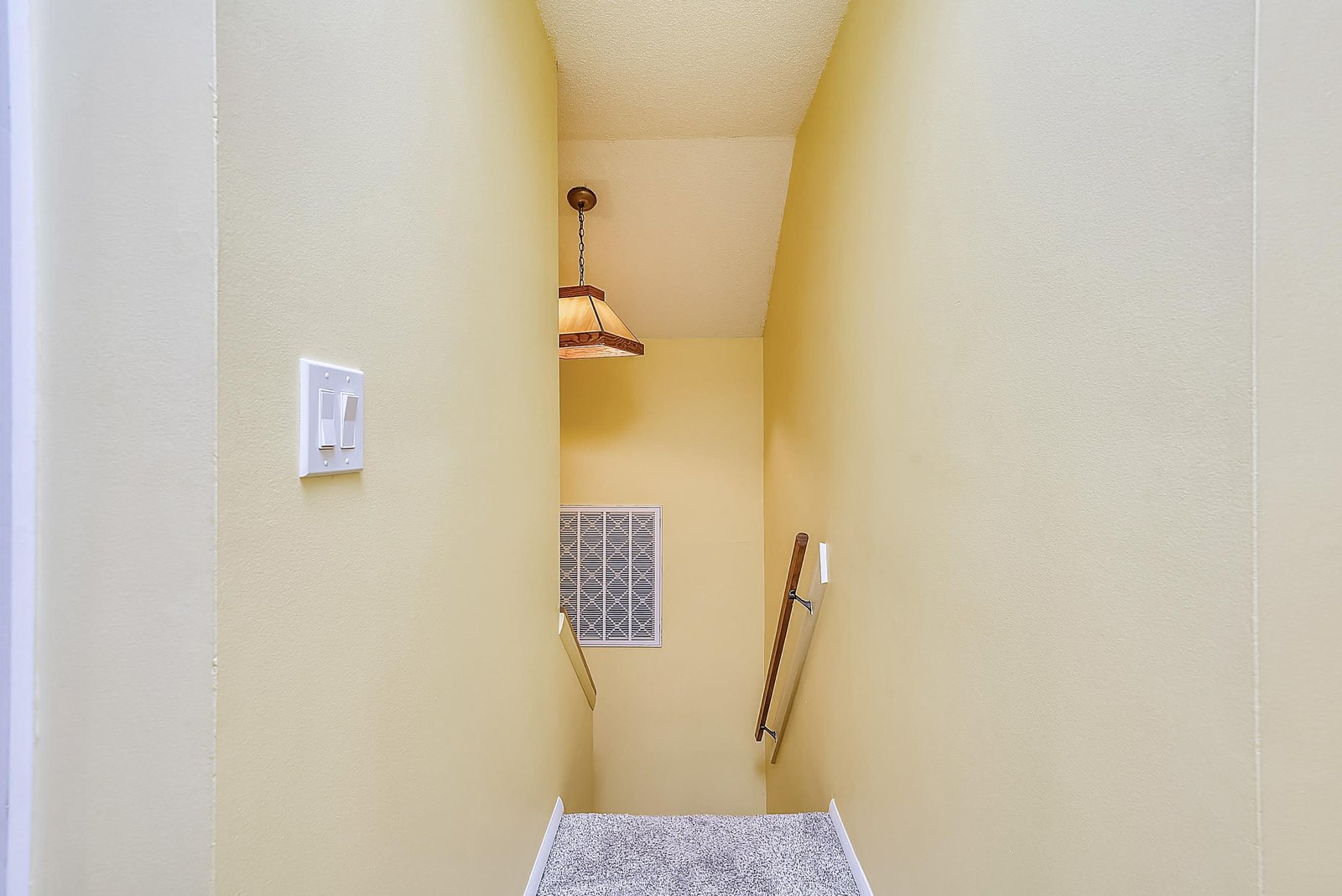 A well-lit stairway features warm yellow walls, modern pendant lighting, and a sturdy handrail to guide you between floors with ease.