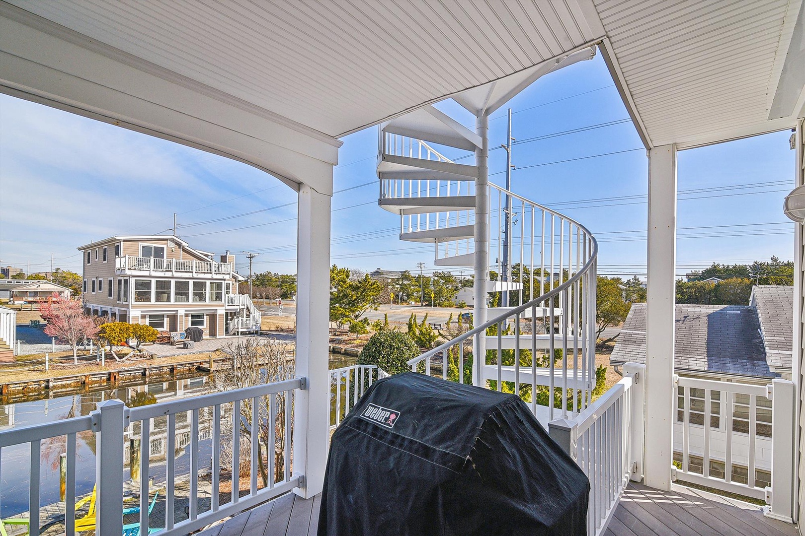 This covered deck features a charming spiral staircase, waterfront views, and a grill perfect for outdoor cooking. The bright, airy space overlooks the neighborhood and nearby water.