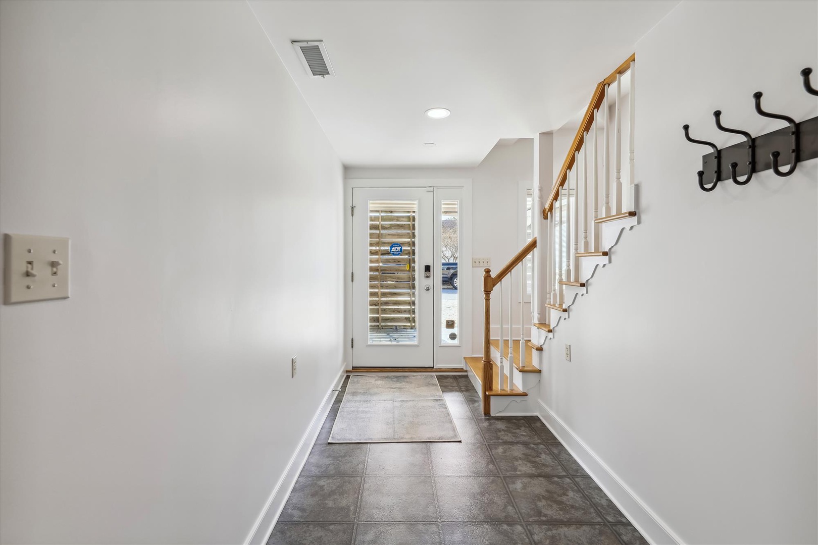 A bright, welcoming entryway with sleek tile floors, warm wood staircase, and convenient wall hooks greets you as you step inside, setting a clean and organized tone for your entire stay.