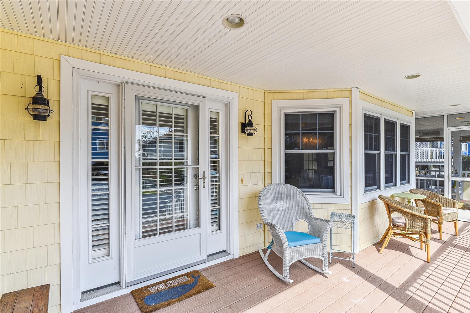 A welcoming covered porch with cheerful yellow siding, wicker seating, and nautical lanterns sets a relaxed coastal tone from the moment you arrive.