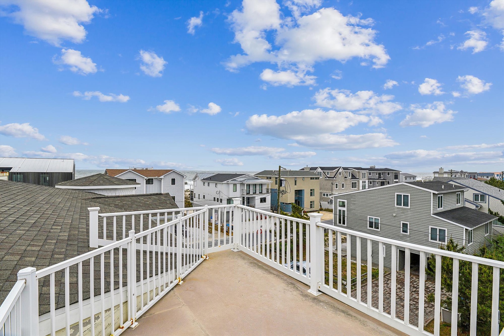Rooftop deck overlooking a quiet residential neighborhood with ocean access nearby. This outdoor space provides open-air relaxation under blue skies and scattered clouds.