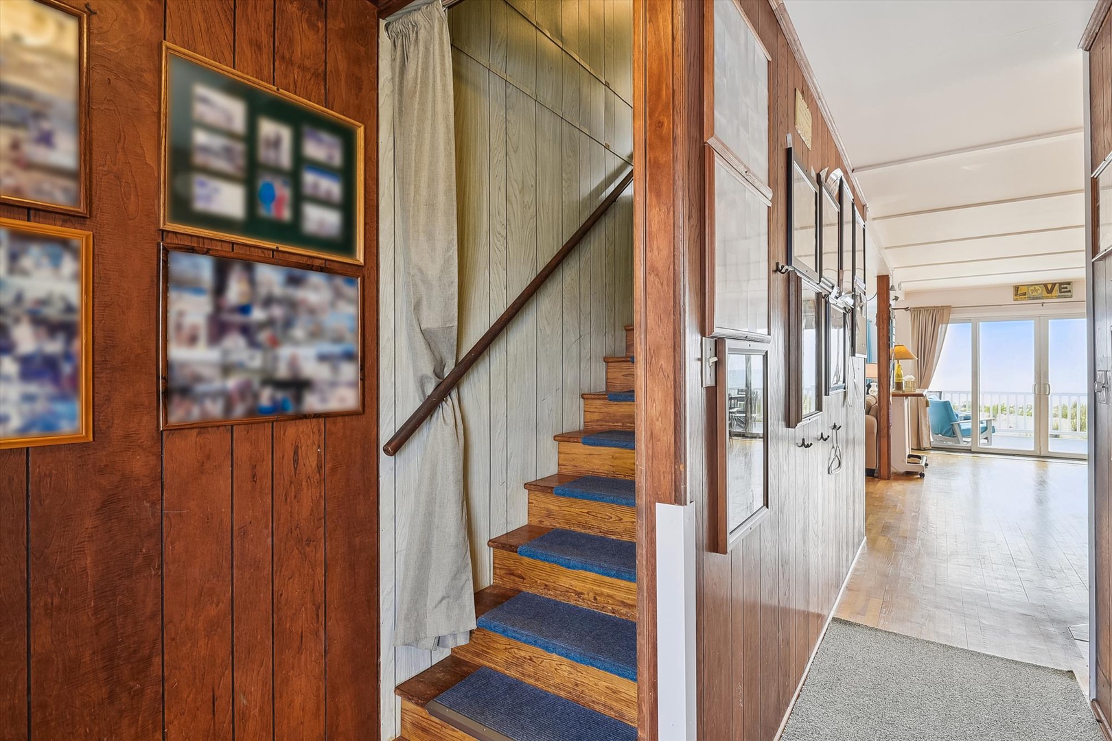 Warm wood-paneled hallway features charming blue-carpeted stairs leading to upper floors, with bright lake views visible beyond.