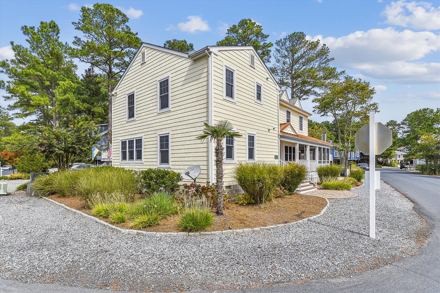 A welcoming two-story coastal home with fresh white siding and natural landscaping, nestled in a peaceful residential area surrounded by tall pines and native greenery.