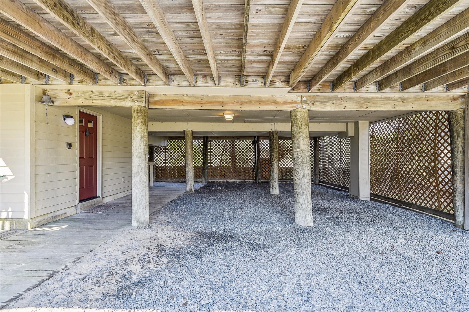 Covered parking area with exposed timber beams and gravel surface, providing secure storage space underneath the elevated property structure.