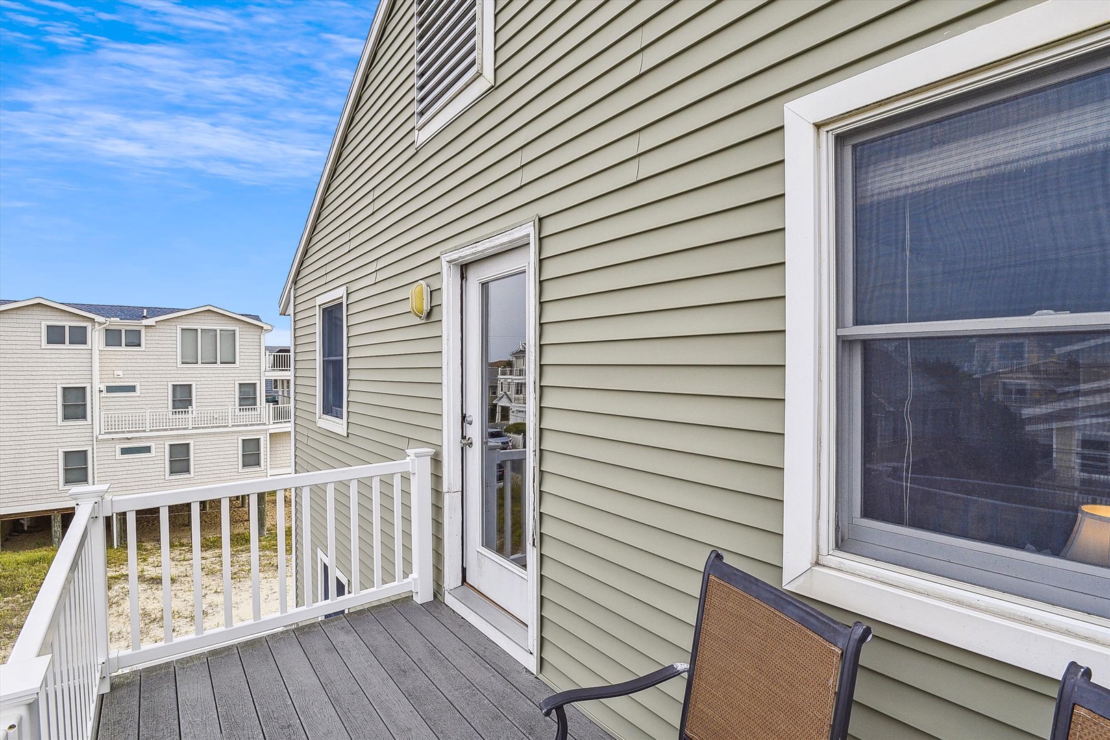 Exterior balcony space featuring beach-style siding, neighboring residential buildings, and clear daytime skies as part of the surrounding coastal neighborhood.