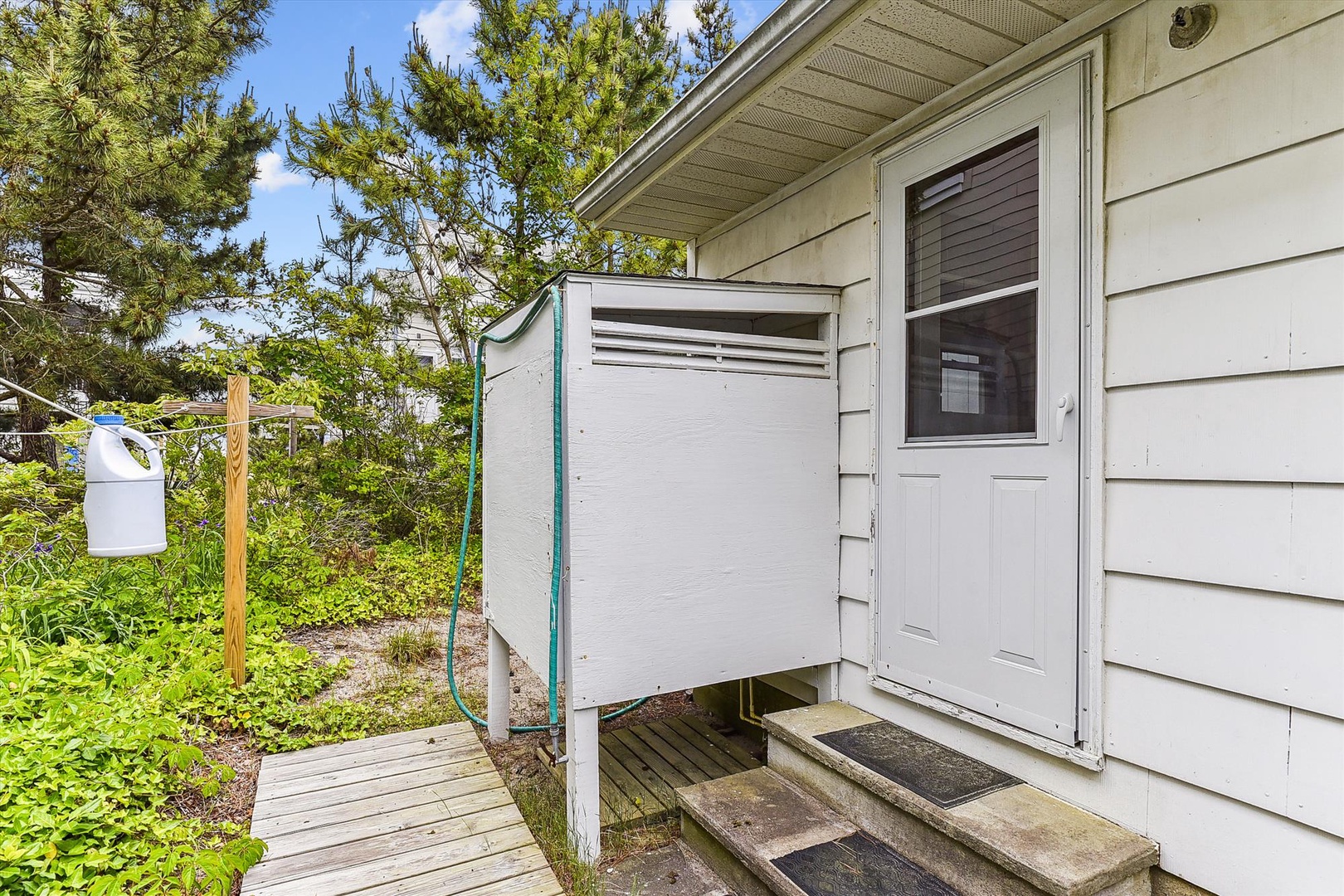 The property features an exterior utility area with an air conditioning unit, ensuring comfort during your stay. The cottage sits nestled among lush greenery and mature trees.