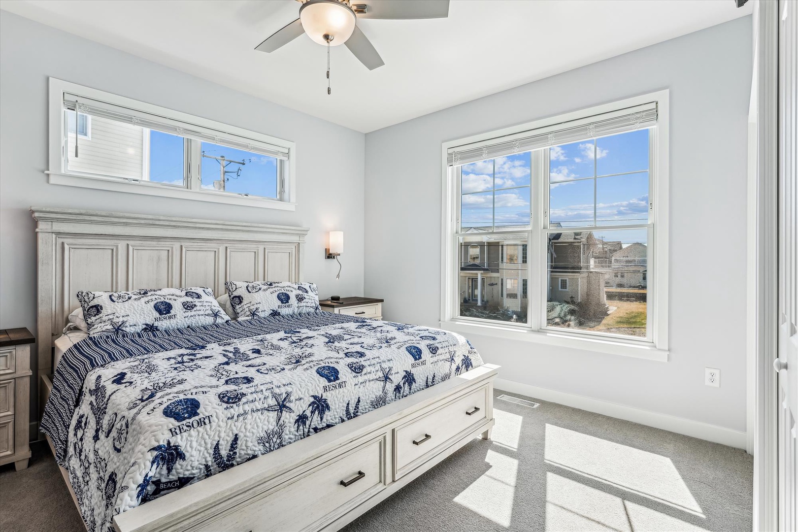 Wake up refreshed in your bright bedroom with coastal charm and peaceful neighborhood views through large windows.