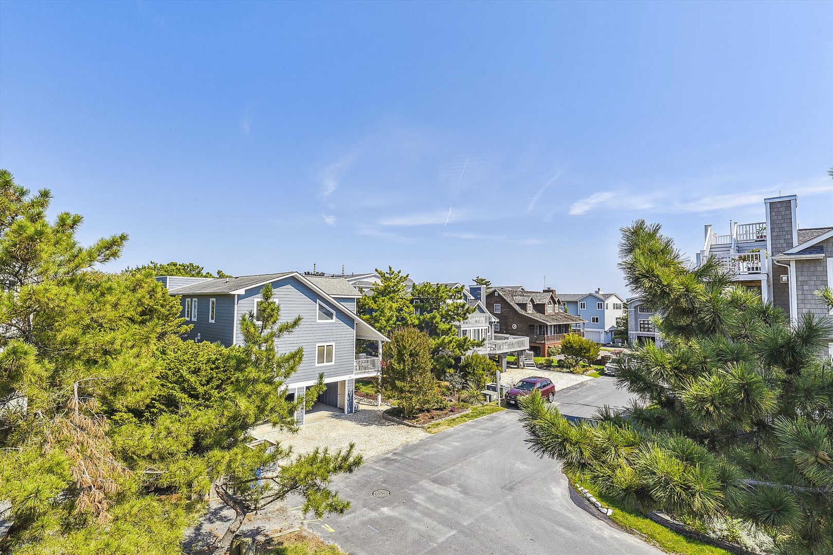 Coastal residential neighborhood with beach-style homes nestled among pine trees and paved access roads, just moments from the shoreline.