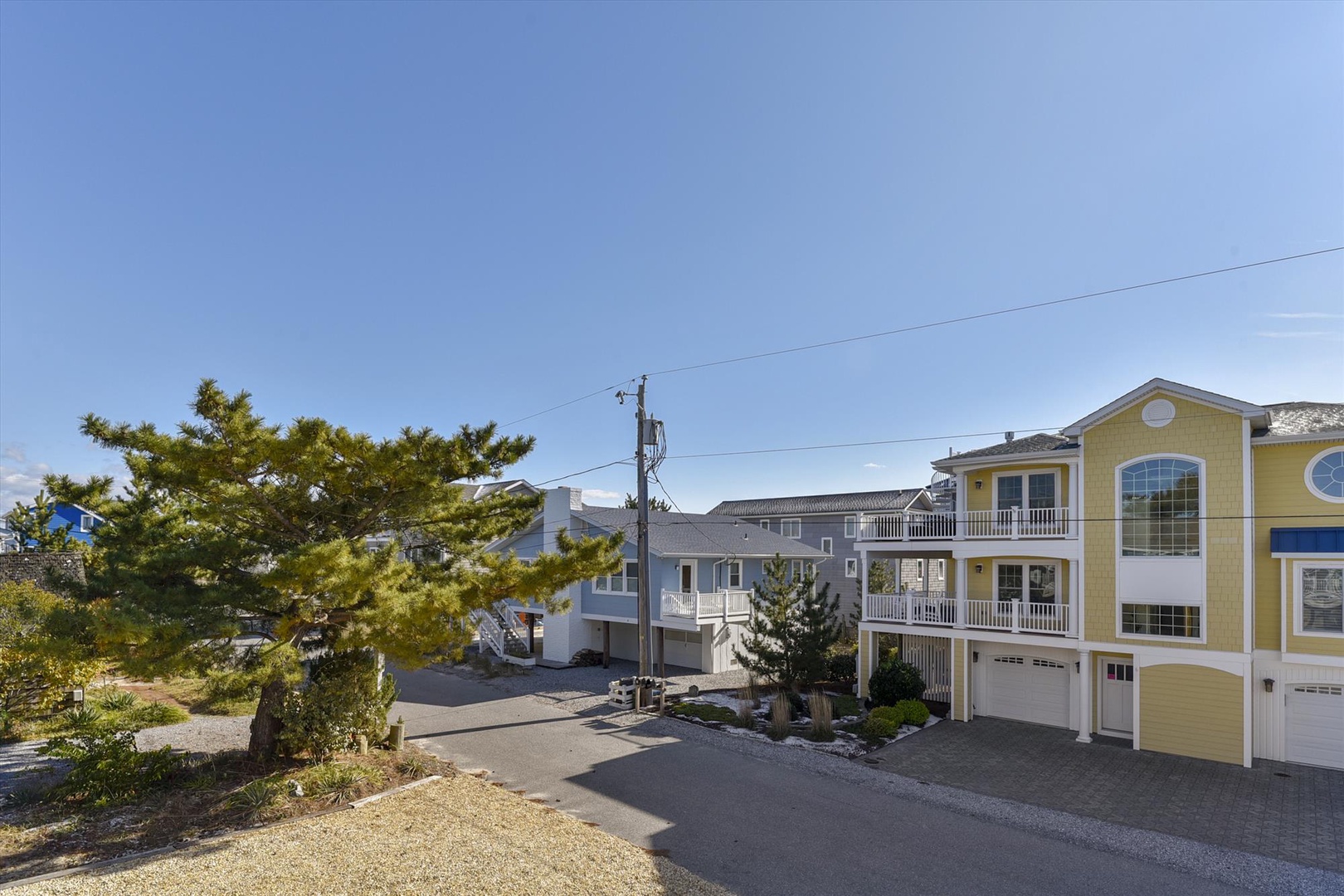 Coastal residential street featuring the property's bright yellow exterior with white trim and nearby beachfront homes surrounded by natural landscaping.