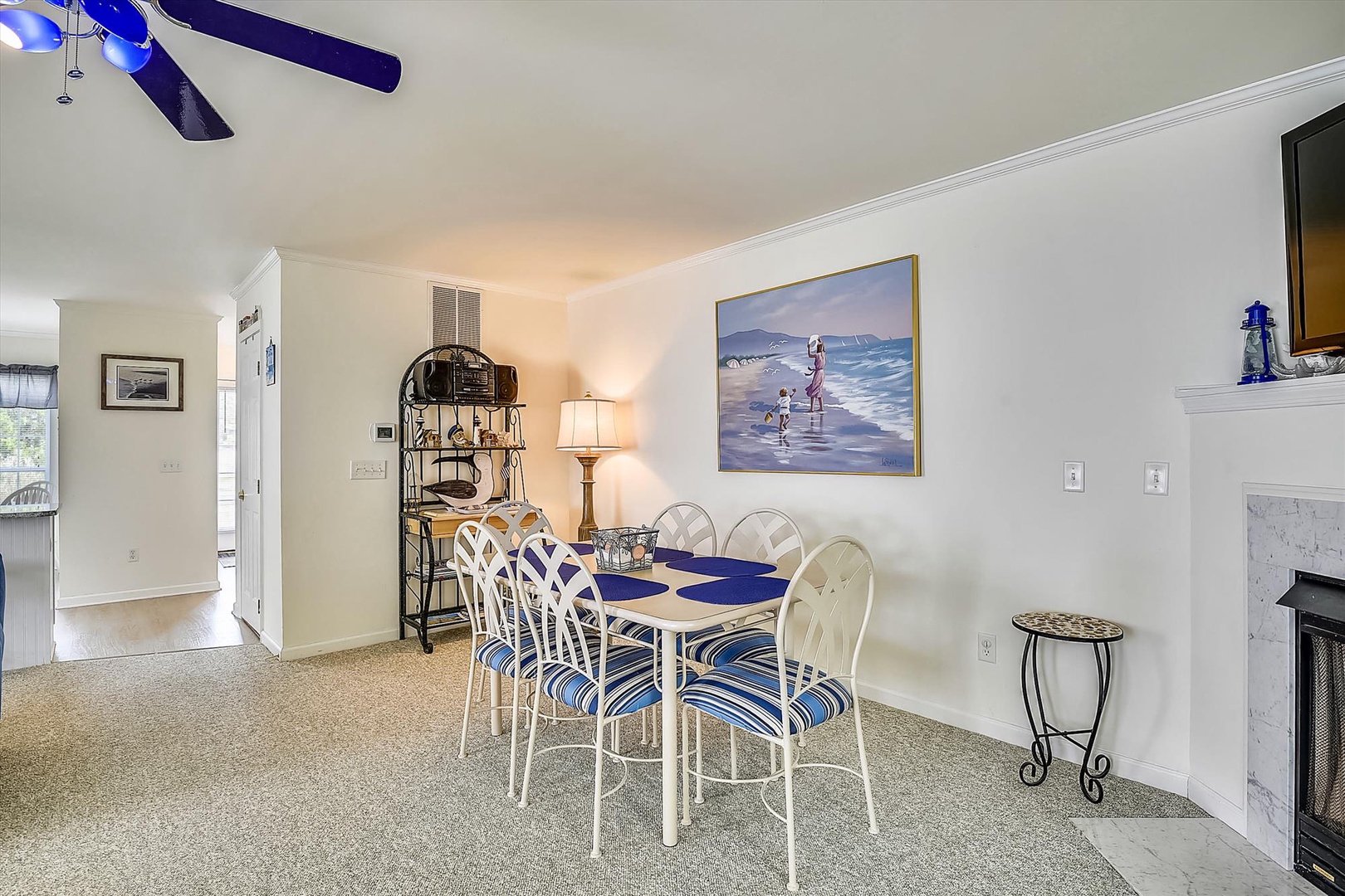 Picture yourself gathering around this cheerful dining table for meals and game nights, with coastal artwork setting a relaxing beach-house vibe and a ceiling fan keeping you comfortable.