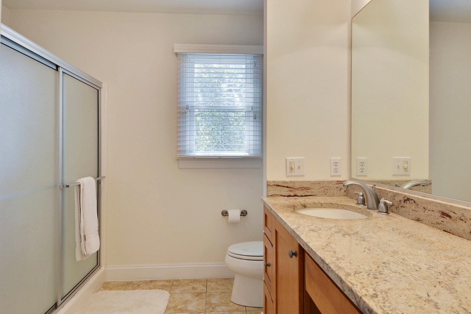 Step into a clean, modern bathroom with a spacious granite countertop, convenient shower, and plenty of natural light to start your mornings right.
