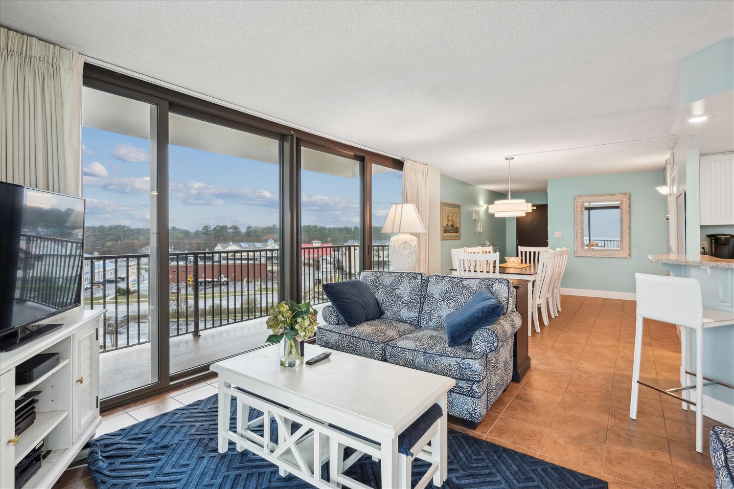 Step into your airy open living space, where soft blues meet crisp whites and sunlight pours through floor-to-ceiling windows. Your private balcony invites morning coffee moments overlooking the peaceful surroundings.