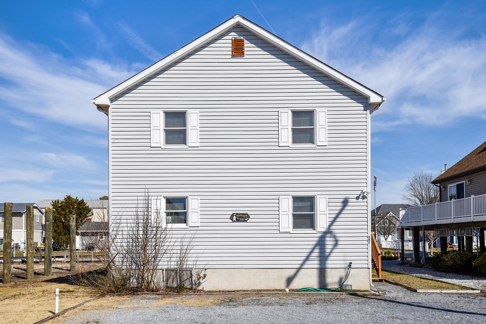 A classic two-story white siding home with shuttered windows stands ready for your beach getaway, offering simple comfort in a friendly coastal neighborhood.