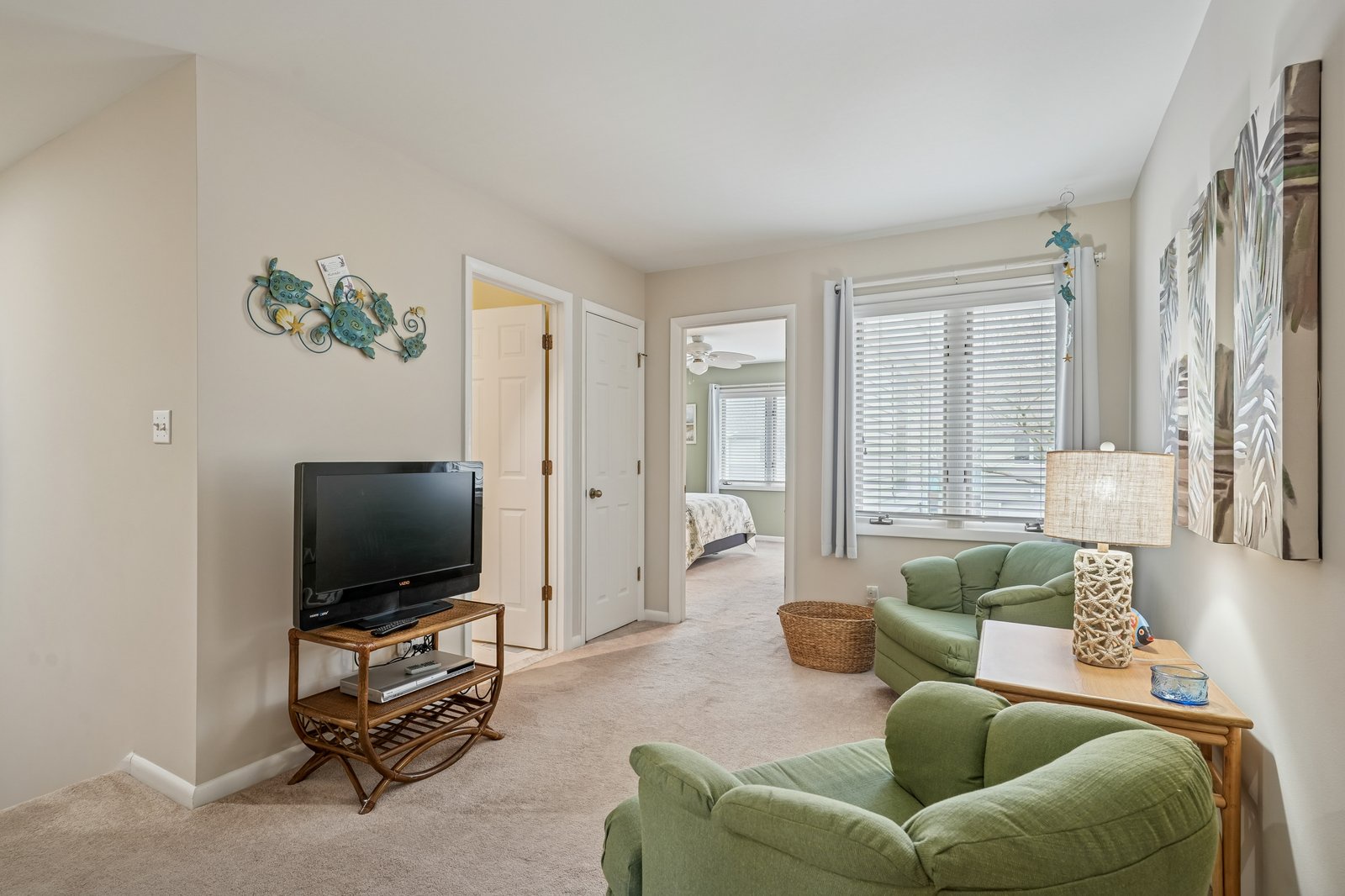 Unwind in your cozy living space featuring comfortable green seating, natural wood accents, and cheerful coastal artwork that creates the perfect retreat atmosphere.