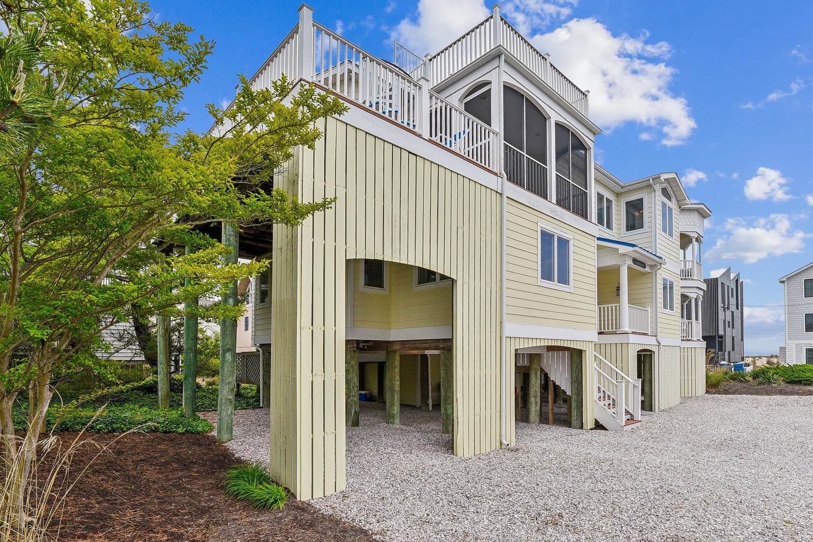 A coastal vacation home featuring multiple elevated decks and balconies, set in a beach community with lush landscaping and convenient parking.