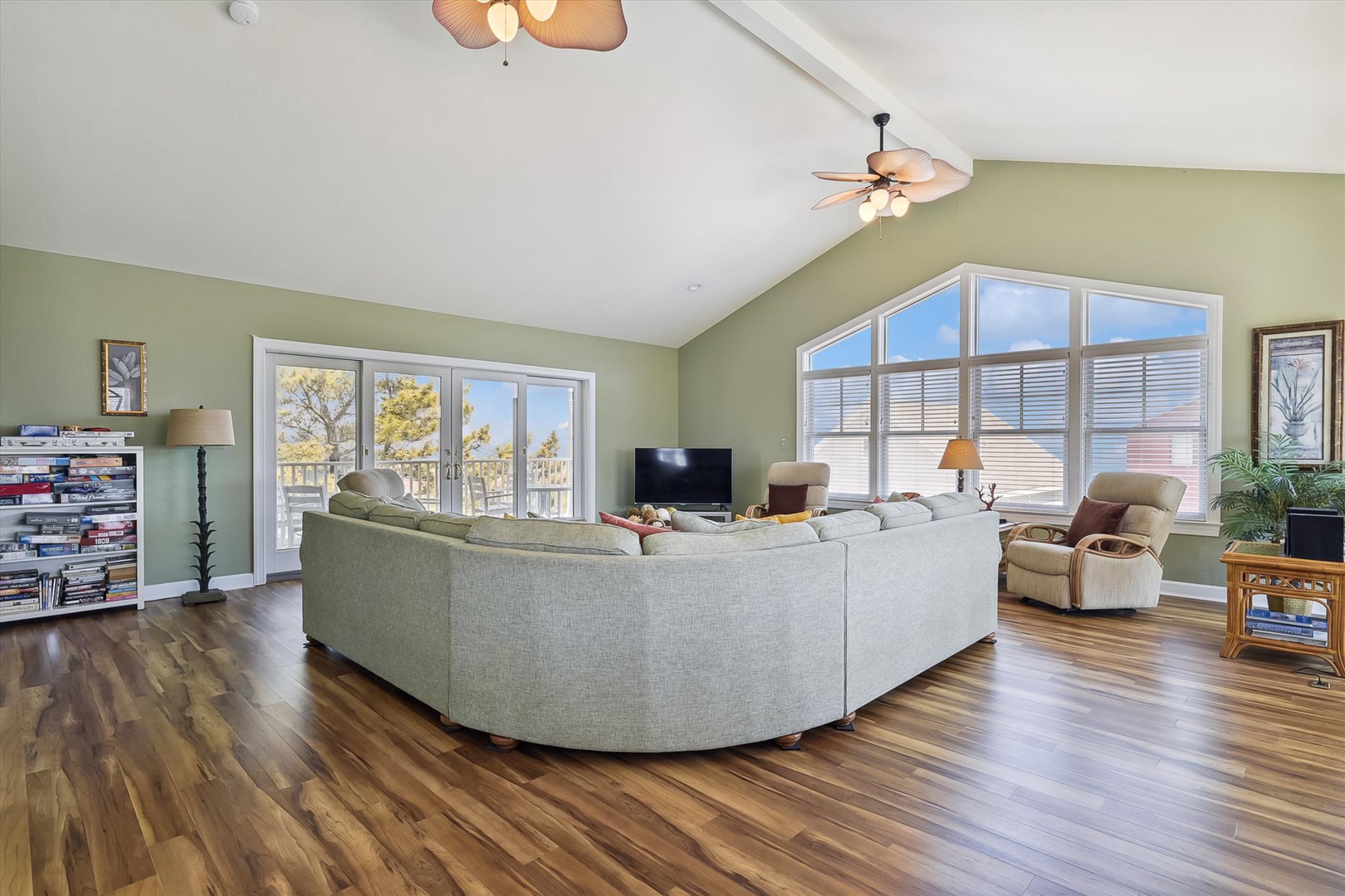 Relax in your spacious living room with vaulted ceilings, warm wood floors, and abundant natural light streaming through oversized windows that frame peaceful outdoor views.