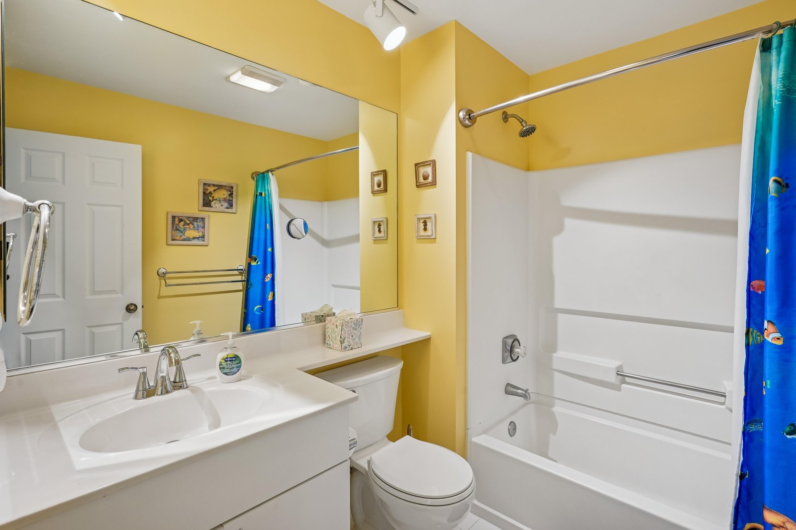 Your cheerful bathroom features sunny yellow walls, a white vanity with modern fixtures, and a tub-shower combo with fun ocean-themed curtain—fresh, bright, and ready for you.