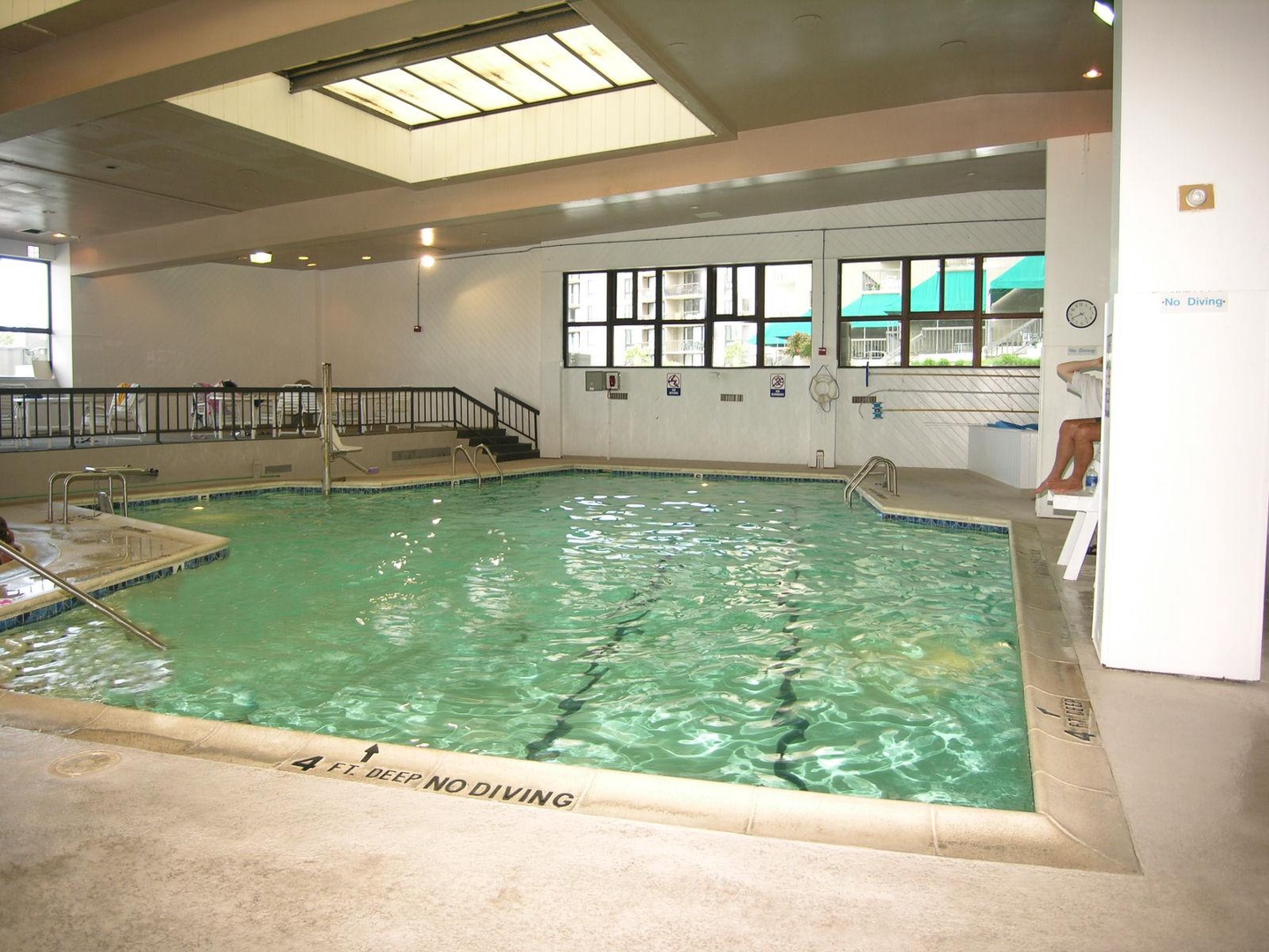 Indoor swimming pool with accessible entry features, skylight, and refreshing turquoise water for year-round enjoyment.