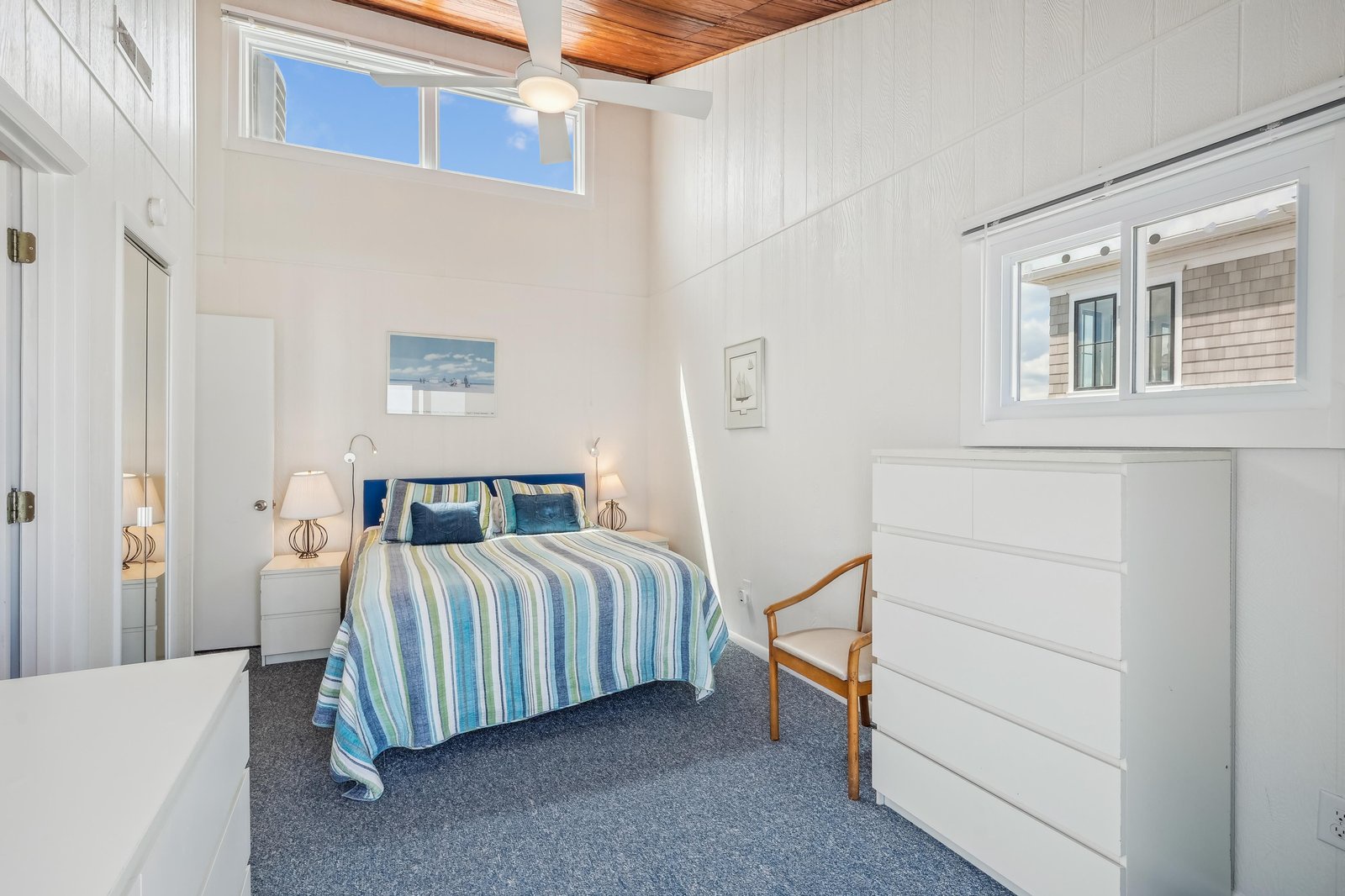 Relax in your coastal-inspired bedroom with vaulted wood ceilings, crisp white shiplap, and soft natural light streaming through high windows—your peaceful retreat after a day of exploring.
