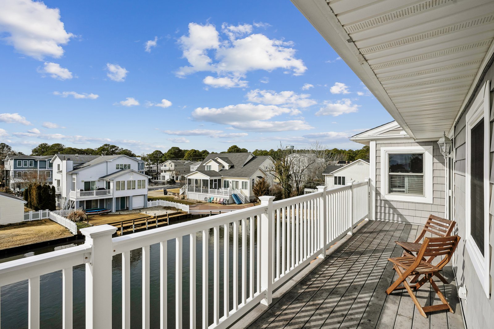 Elevated balcony deck with wooden chairs overlooking a peaceful residential neighborhood under bright blue skies.