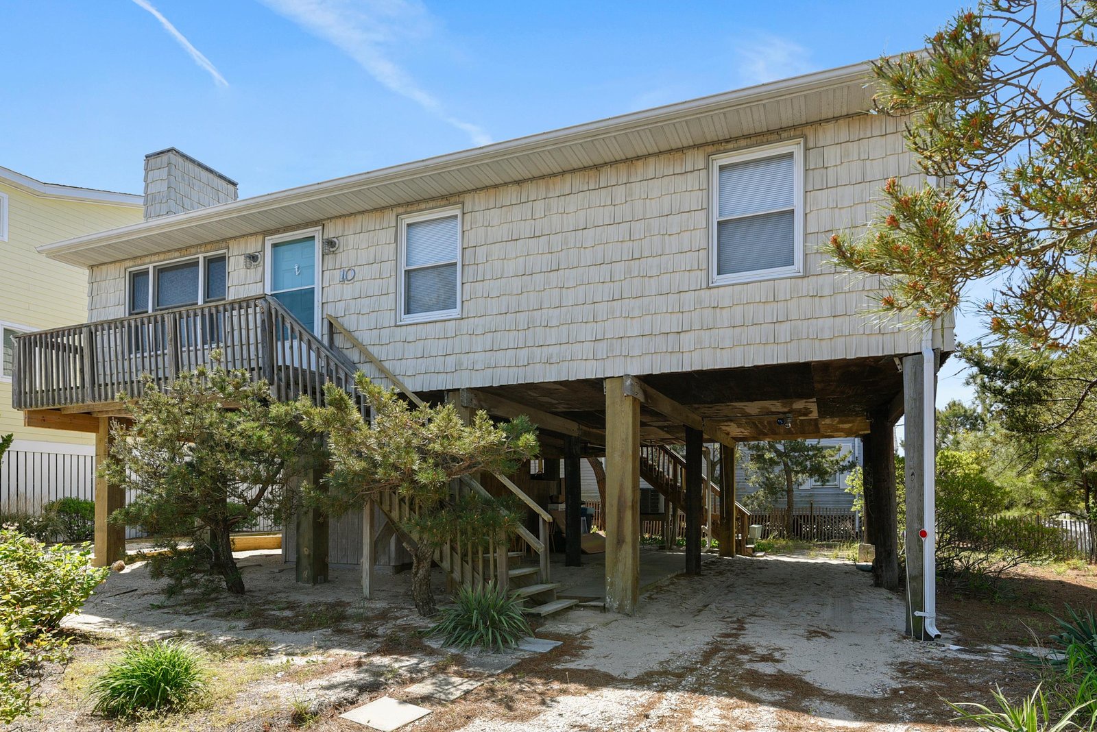 A classic beach house elevated on sturdy pilings, surrounded by coastal greenery and offering easy access to sandy shores.