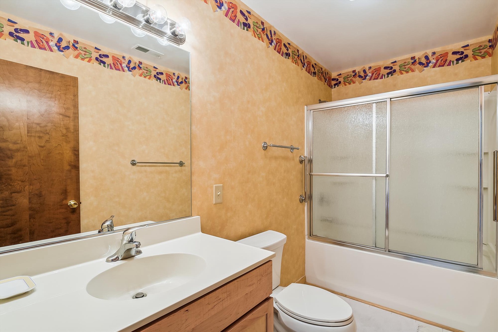 Warm, welcoming bathroom with plenty of counter space, a tub-shower combo, and charming decorative tile accents at eye level to brighten your morning routine.