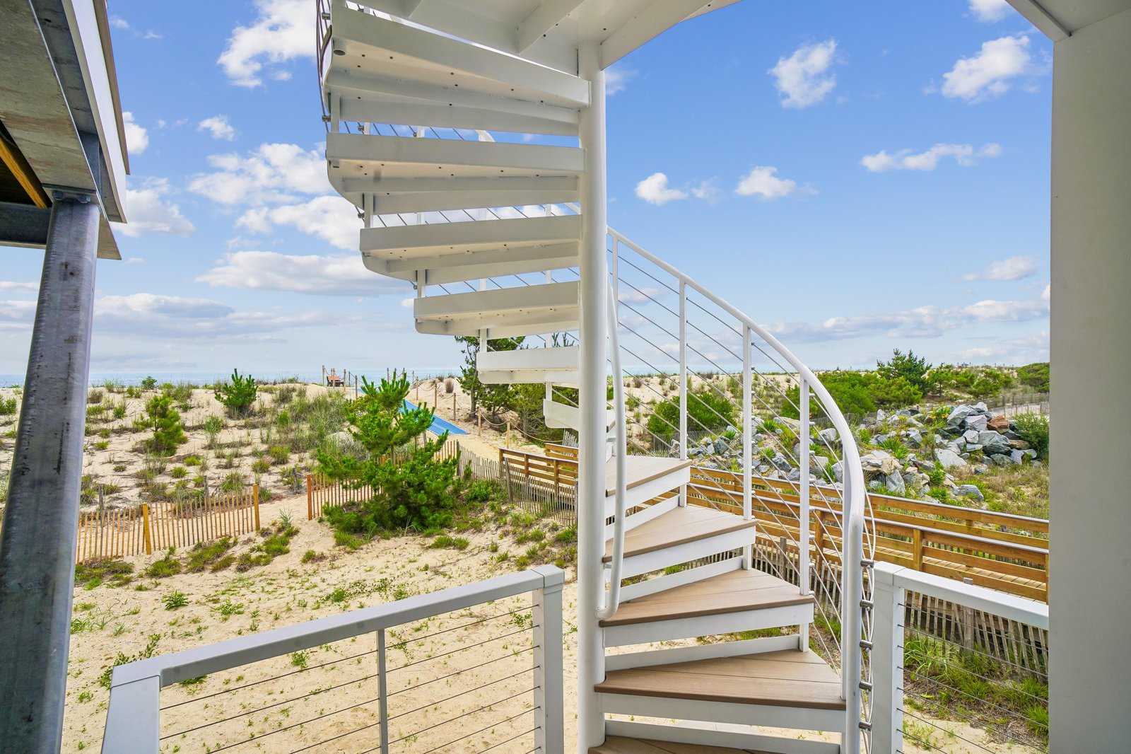 A bright spiral staircase connects multiple levels of this coastal property, surrounded by natural dunes and native greenery. Your beachside escape blends modern design with unspoiled nature.