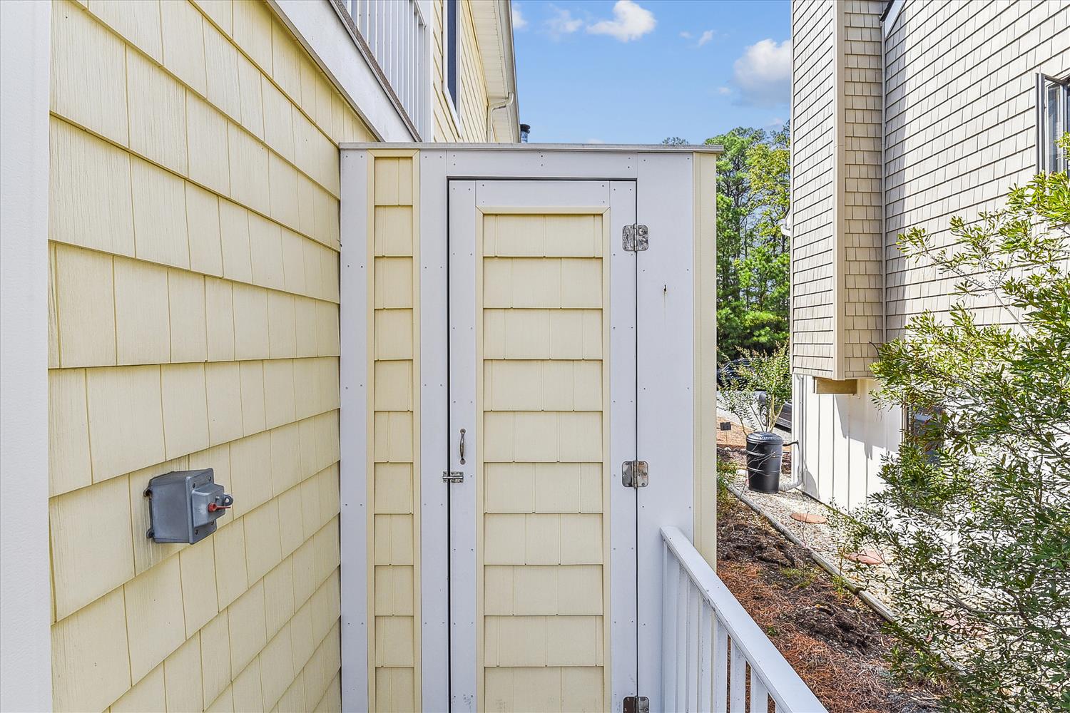 The property features a quiet side yard area with outdoor storage and mature landscaping, situated in a residential neighborhood beneath clear blue skies.