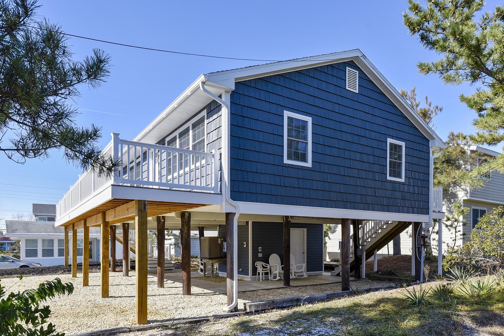 Charming coastal cottage with blue shingle siding surrounded by mature trees in a peaceful neighborhood setting.