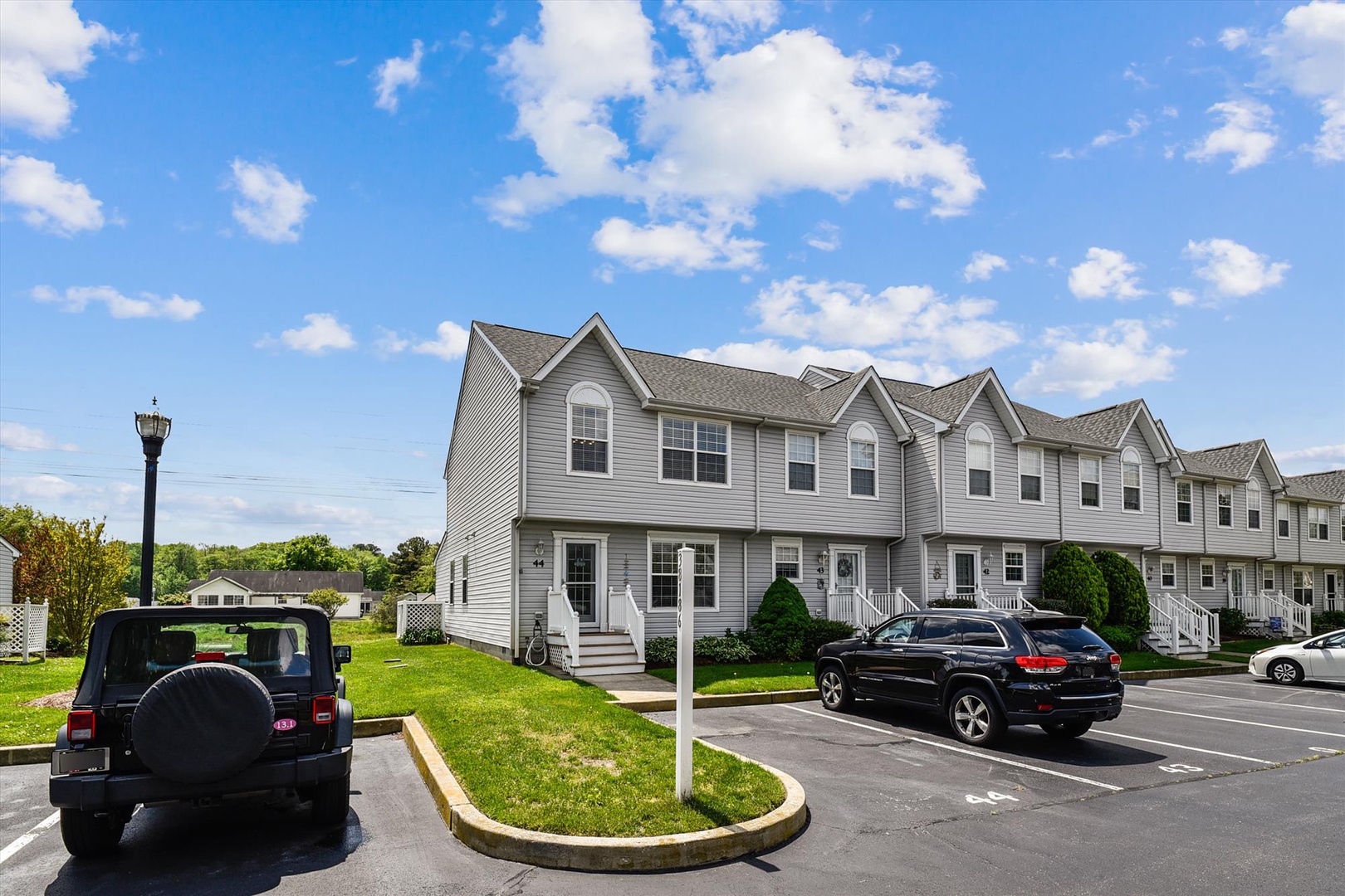 A row of townhomes with dedicated parking spaces and manicured landscaping under a bright, cloud-dotted sky.