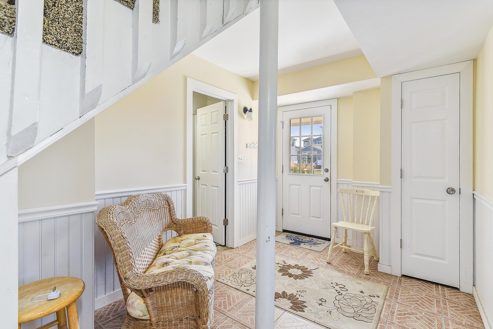 Step into your cheerful cottage entrance, where soft yellow walls and a cozy wicker chair invite you to pause and settle in after a day of exploring.