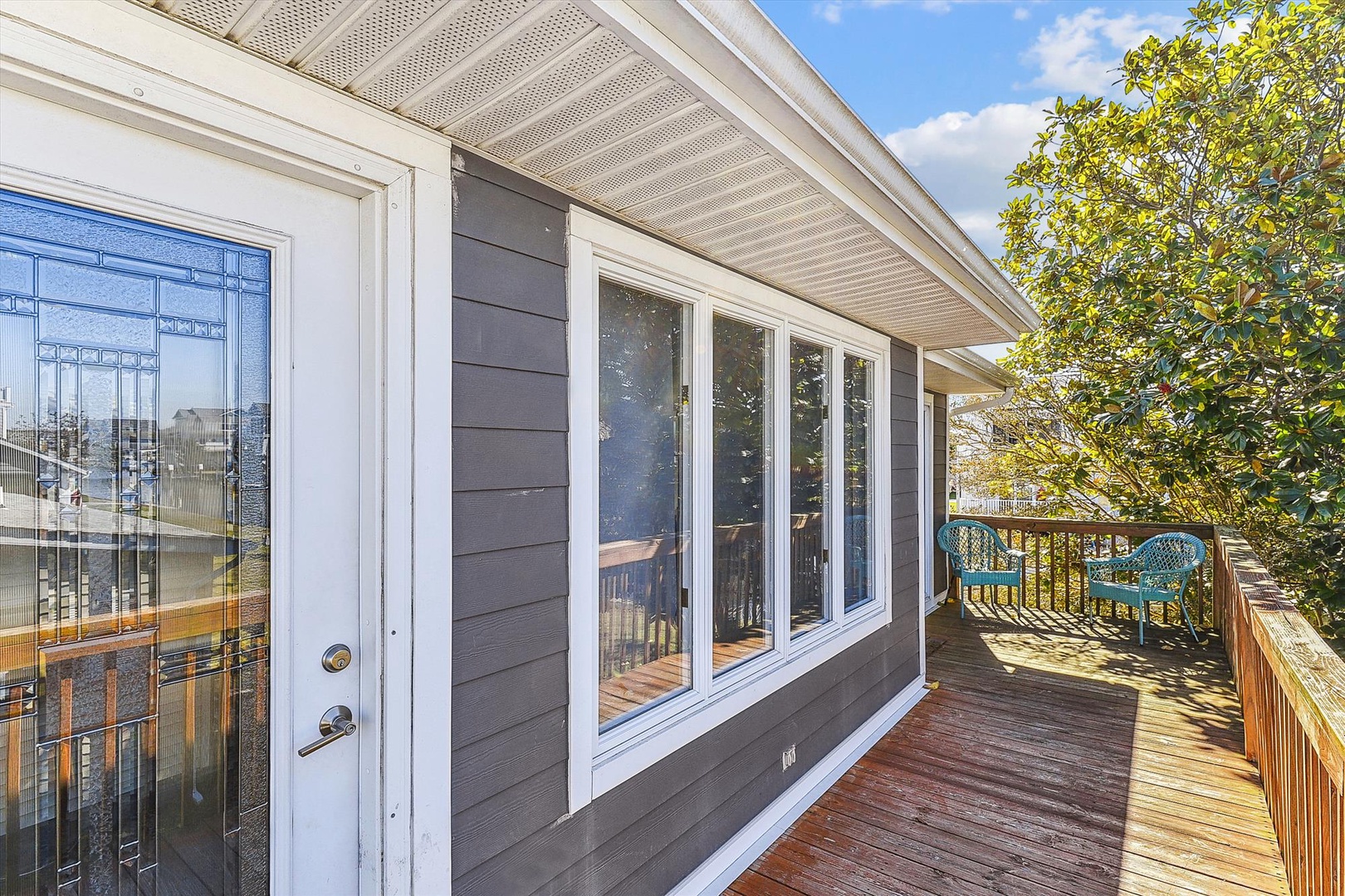Sunlit deck with charming patio furniture awaits, framed by lush greenery and a bright blue sky—ideal for your morning coffee or evening unwind.